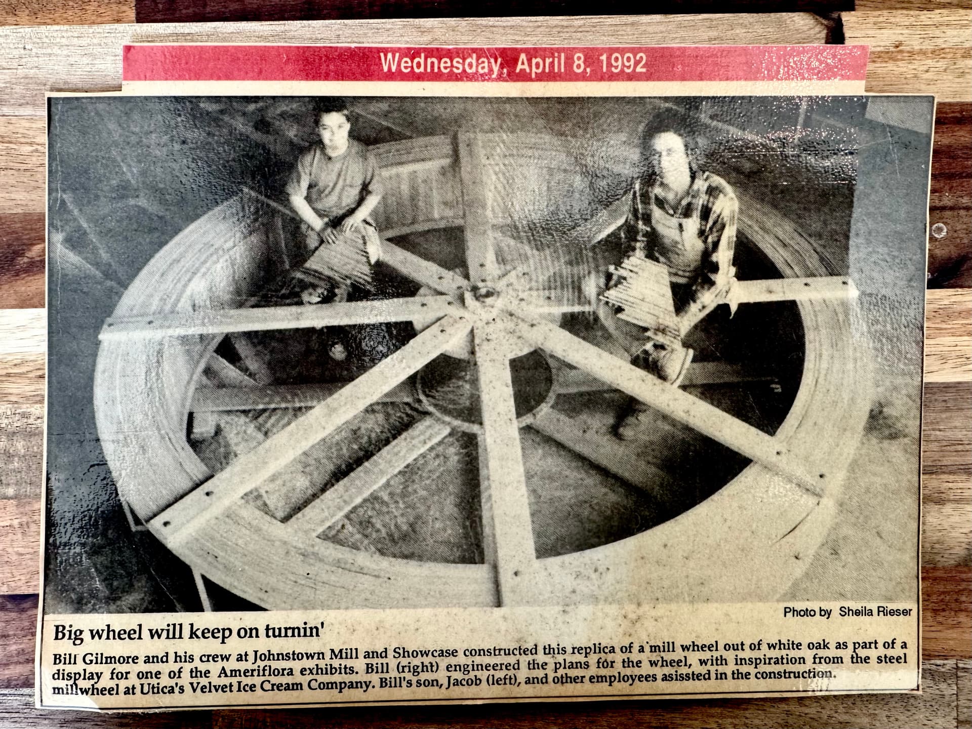 Newspaper clipping: Bill Gilmore and his son Jacob seated on the finished mill wheel in the shop
